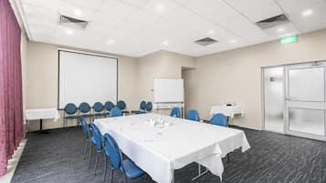 Een vergaderzaal met een lange tafel, stoelen, een whiteboard en een projectiescherm.