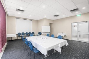 A conference room with a long table, chairs, a whiteboard, and a projector screen.