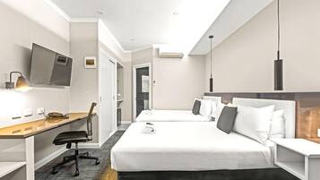 A hotel room with a desk, two beds, a TV, and a modern pendant light.
