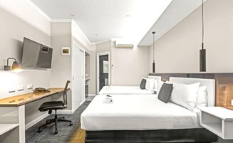 A hotel room with a desk, two beds, a TV, and a modern pendant light.