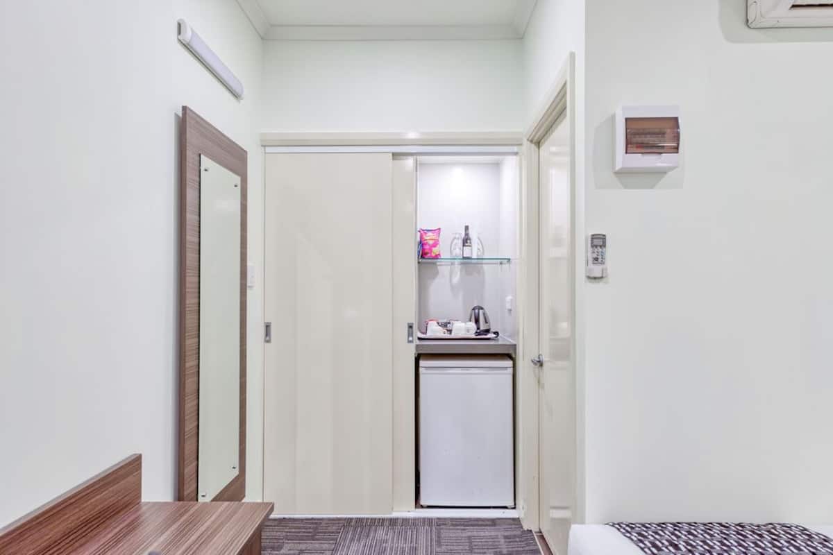 Habitación de hotel con un banco de madera, una kitchenette pequeña con refrigerador, microondas y cafetera.