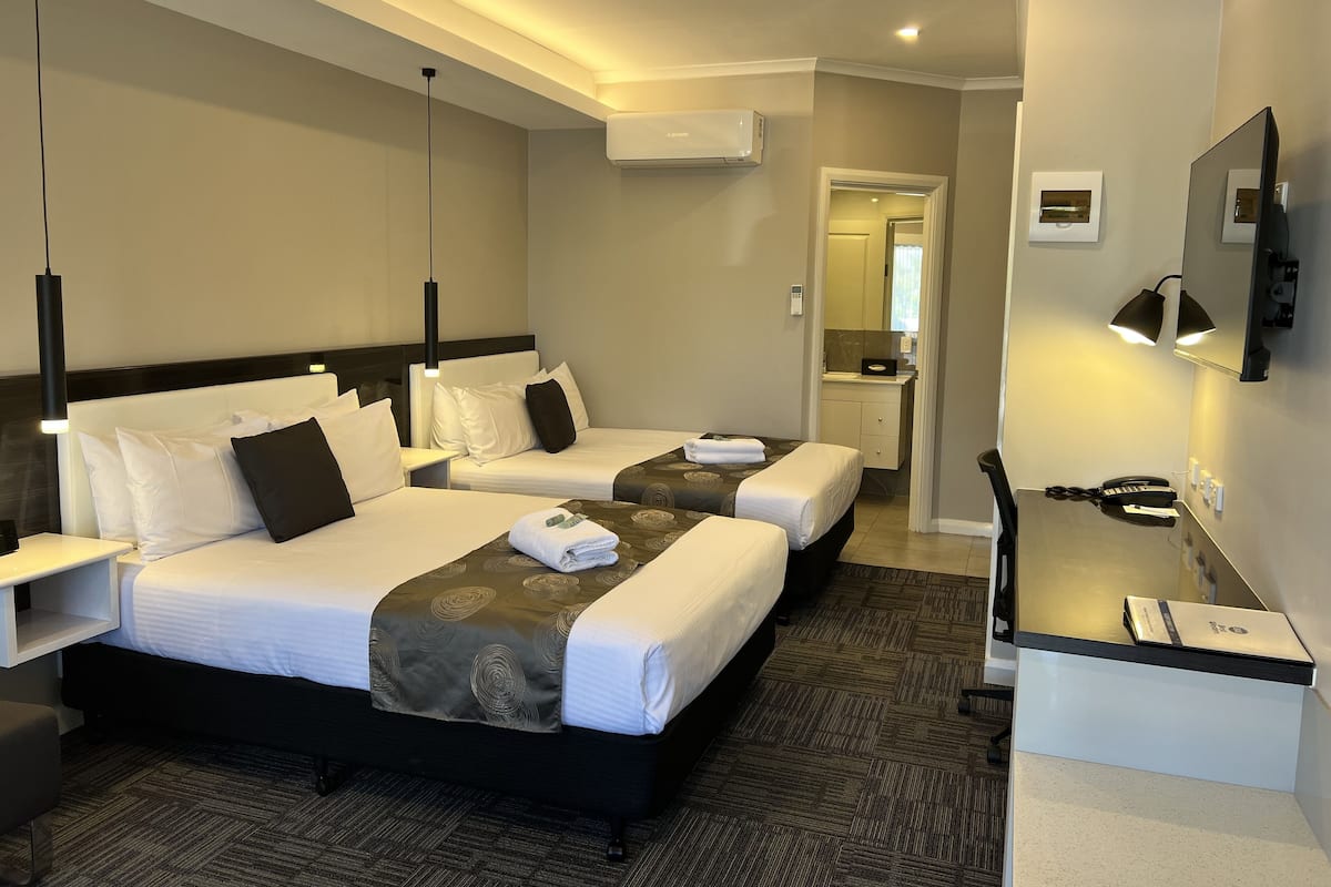 Habitación de hotel con dos camas, un escritorio, una silla, un televisor y un aire acondicionado.