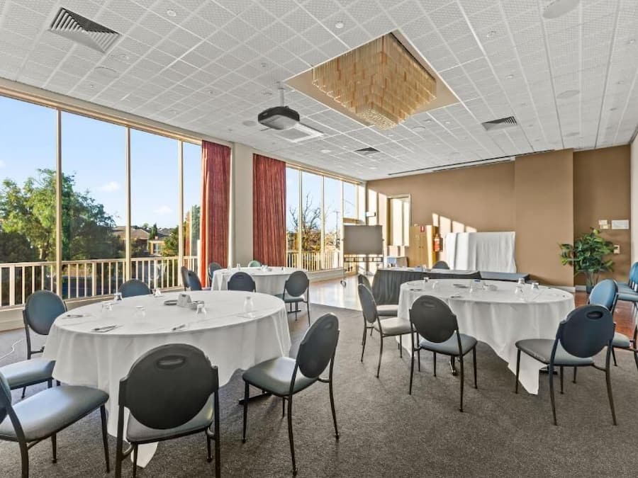 Ein Konferenzraum mit runden Tischen, Stühlen und einem großen Fenster mit Blick auf Bäume.