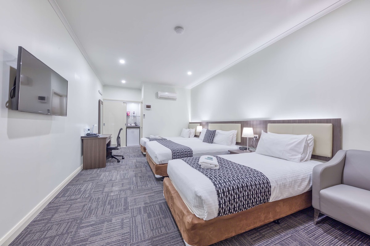 Une chambre d’hôtel avec deux lits, un bureau, une chaise et un téléviseur fixé au mur.