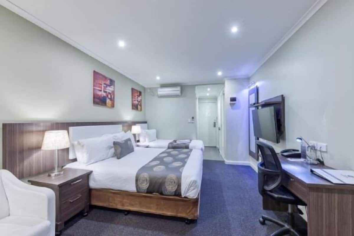 Habitación de hotel con cama, mesitas de noche, escritorio, silla, televisor y aire acondicionado.