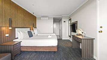 Quarto de hotel com duas camas, uma escrivaninha, uma televisão e um guarda-roupa.
