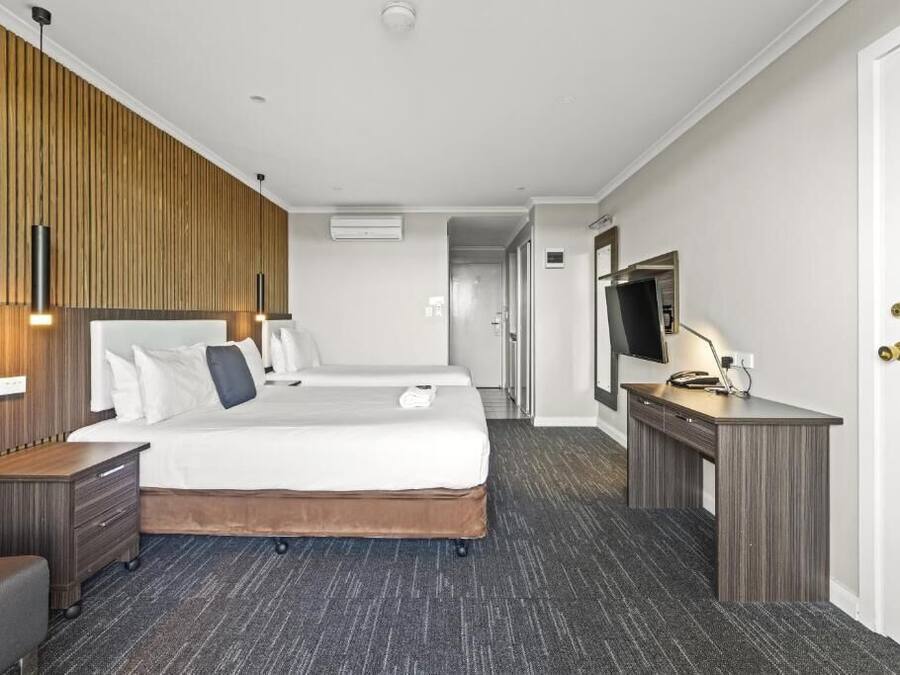 Quarto de hotel com duas camas, uma escrivaninha, uma televisão e um guarda-roupa.