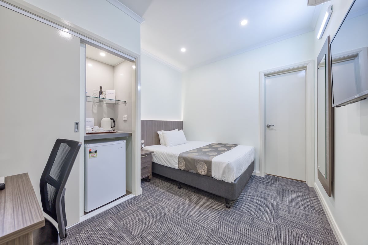 Una habitación de hotel con cama, escritorio, refrigerador pequeño y una silla.