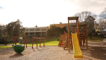Kids can play on the playground's ball pit, slide, and climbing frame amidst trees and grass.