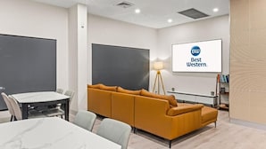 Ein Konferenzraum mit einem großen Tisch, einer Couch, einer Projektionsleinwand und einem Schild mit der Aufschrift 'Best Western'.