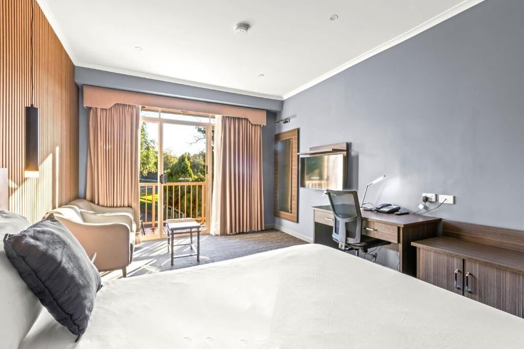 Quarto de hotel com cama, escrivaninha, cadeira e varanda com cortinas.