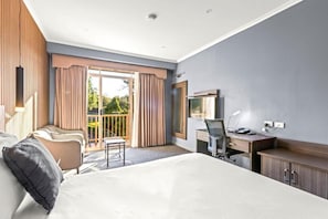 Ein Hotelzimmer mit Bett, Schreibtisch, Stuhl und einem Balkon mit Vorhängen.