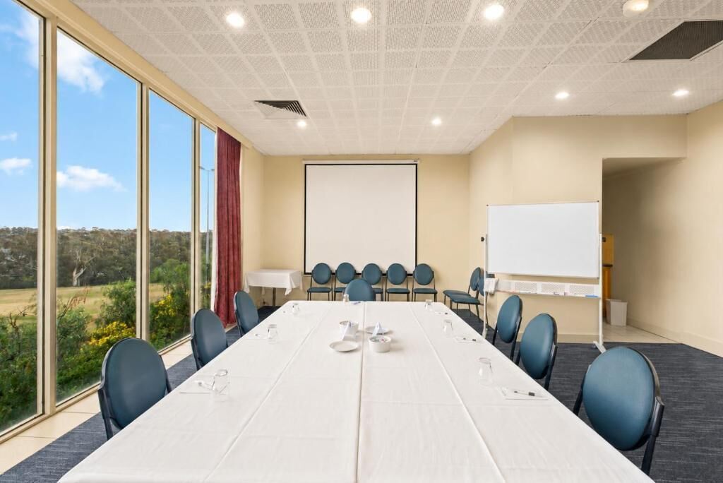 A conference room with a long table, chairs, a whiteboard, and a projector screen.