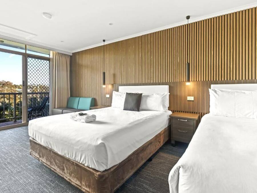 A hotel room with a large bed, a nightstand, a chair, and a view of the outdoors.