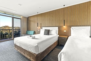 Habitación de hotel con una cama grande, una mesita de noche, una silla y vistas al exterior.