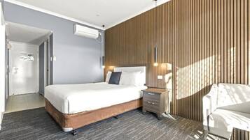 A modern hotel room with a large bed, a bedside table, a chair, and a wooden panel wall.