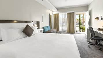A hotel room with a large bed, a desk, a chair, and a view of the outdoors through a door.