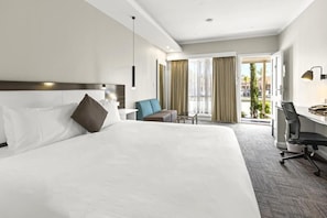 Ein Hotelzimmer mit einem großen Bett, einem Schreibtisch, einem Sessel und Blick ins Freie durch eine Tür.