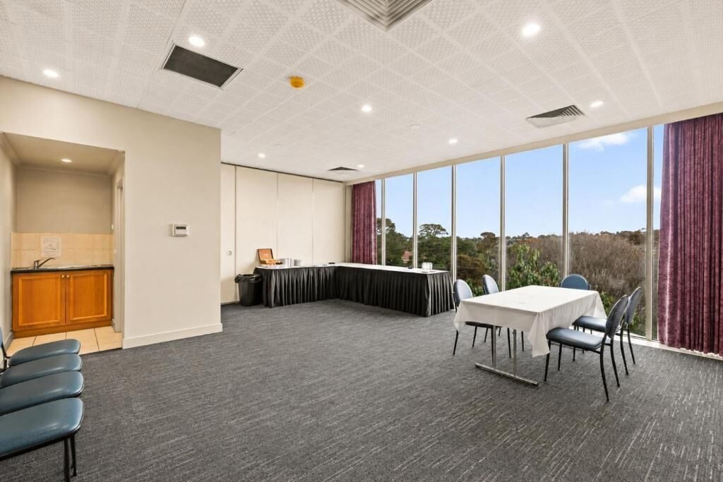 A conference room with a table and chairs, a small kitchenette, and large windows with curtains.