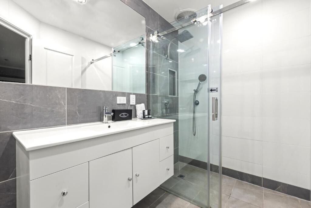 A modern bathroom with a glass-enclosed shower, a white vanity with a sink, and a mirror.