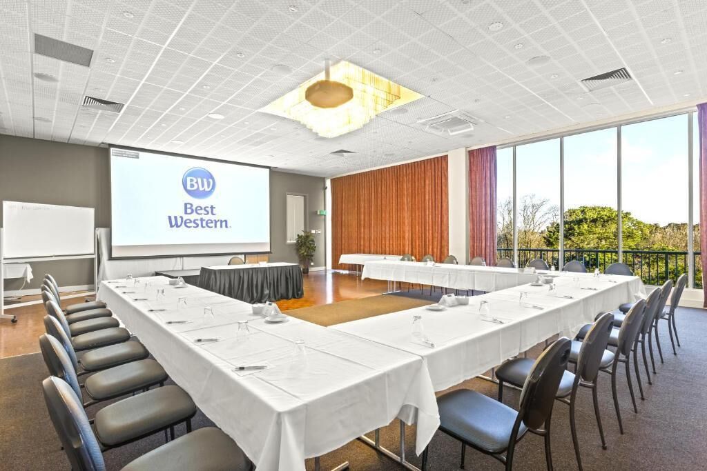 A conference room with a long table, chairs, a projector screen, and a view of the outdoors.