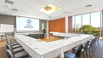 A conference room with a long table, chairs, a projector screen, and a view of the outdoors.