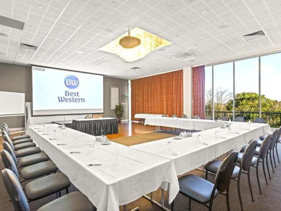 A conference room with a long table, chairs, a projector screen, and a view of the outdoors.