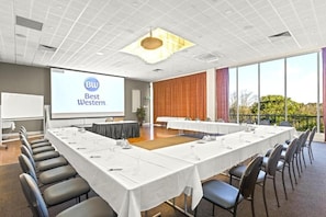 Une salle de conférence équipée d’une longue table, de chaises, d’un écran de projection et offrant une vue sur l’extérieur.