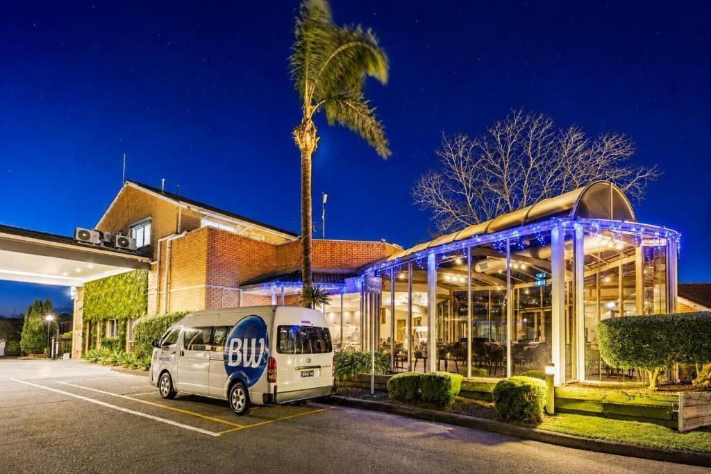 A building with a covered outdoor area, a van with 'BW' branding, and a palm tree.
