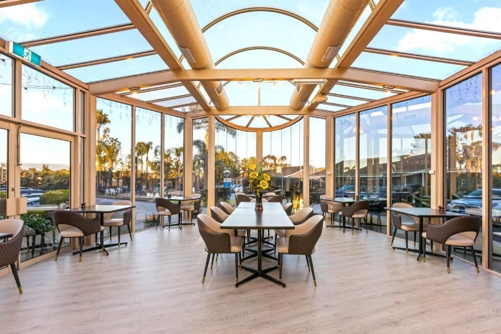 A spacious indoor area with a glass ceiling, multiple tables and chairs, and a view of the outdoors.