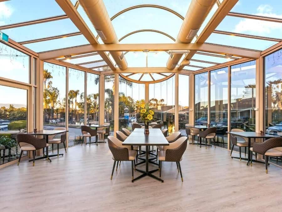 A spacious indoor area with a glass ceiling, multiple tables and chairs, and a view of the outdoors.