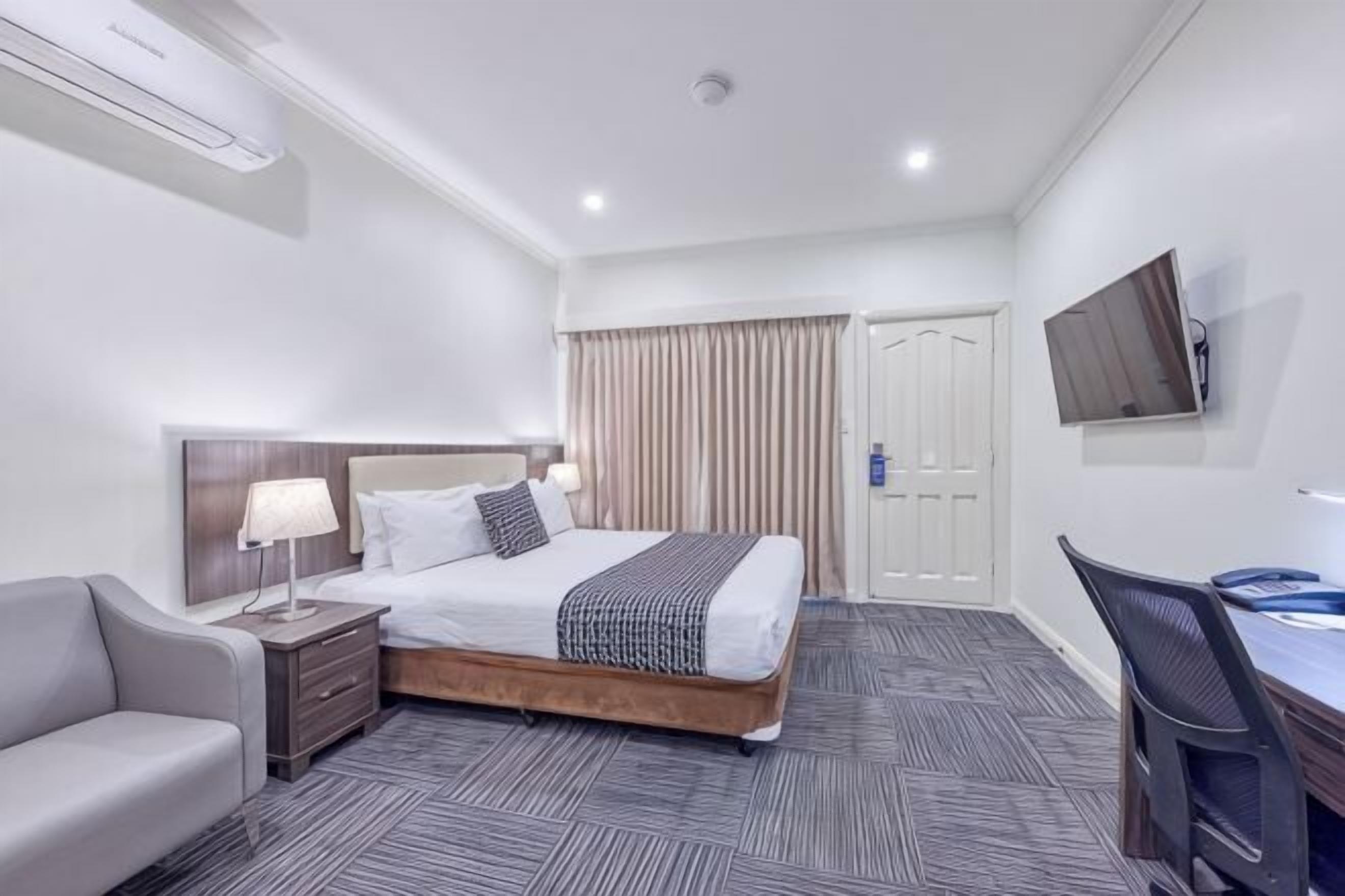 Una habitación de hotel con cama, mesitas de noche, escritorio, silla, televisor y armario.
