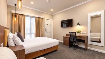 A hotel room with a bed, desk, chair, and a large mirror.