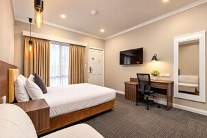 Una habitación de hotel con cama, escritorio, silla y un espejo grande.