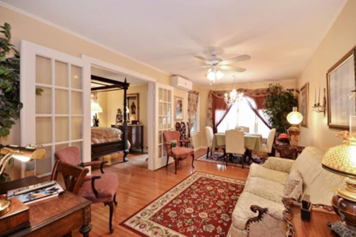 Un salon spacieux doté d’un ventilateur de plafond, d’un tapis aux motifs rouges et blancs et d’un piano.