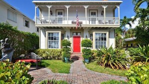A two-story white house with a red door, a balcony, and a garden with a statue and potted plants. - Sabal Palm House Bed & Breakfast (Lake Worth)