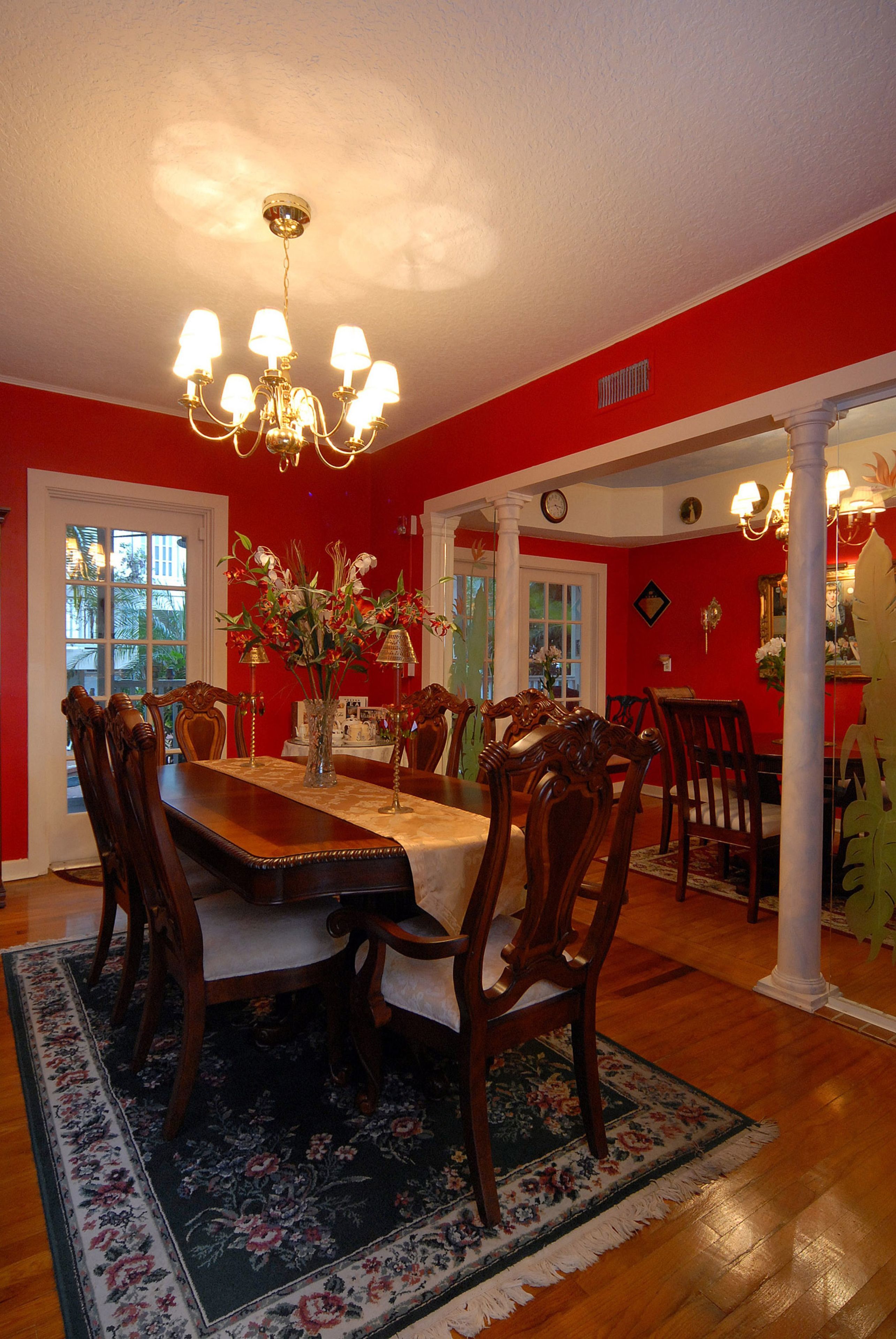 A dining room with a wooden table, chairs, and a chandelier. There is a vase with flowers on the table.