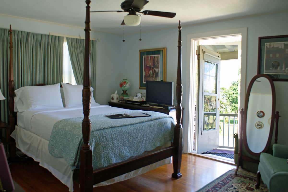 Un lit à baldaquin avec un ventilateur de plafond, un téléviseur posé sur un meuble et une porte donnant sur un balcon.