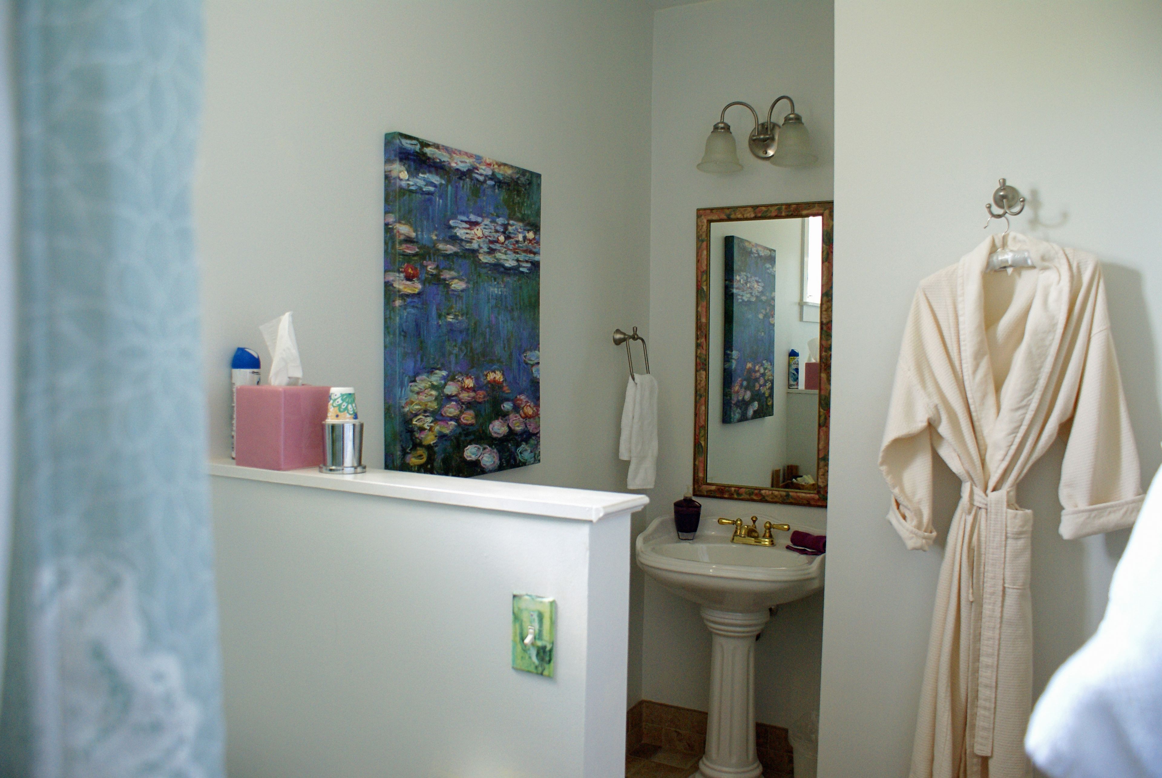 A bathroom with a sink, a painting, a robe, and a mirror.