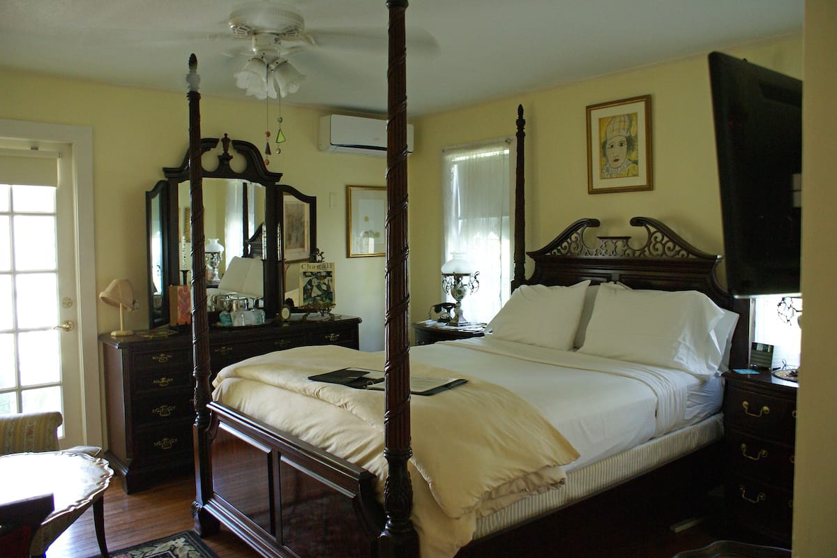 Un lit à baldaquin, une commode en bois, un miroir et un tableau encadré accroché au mur.