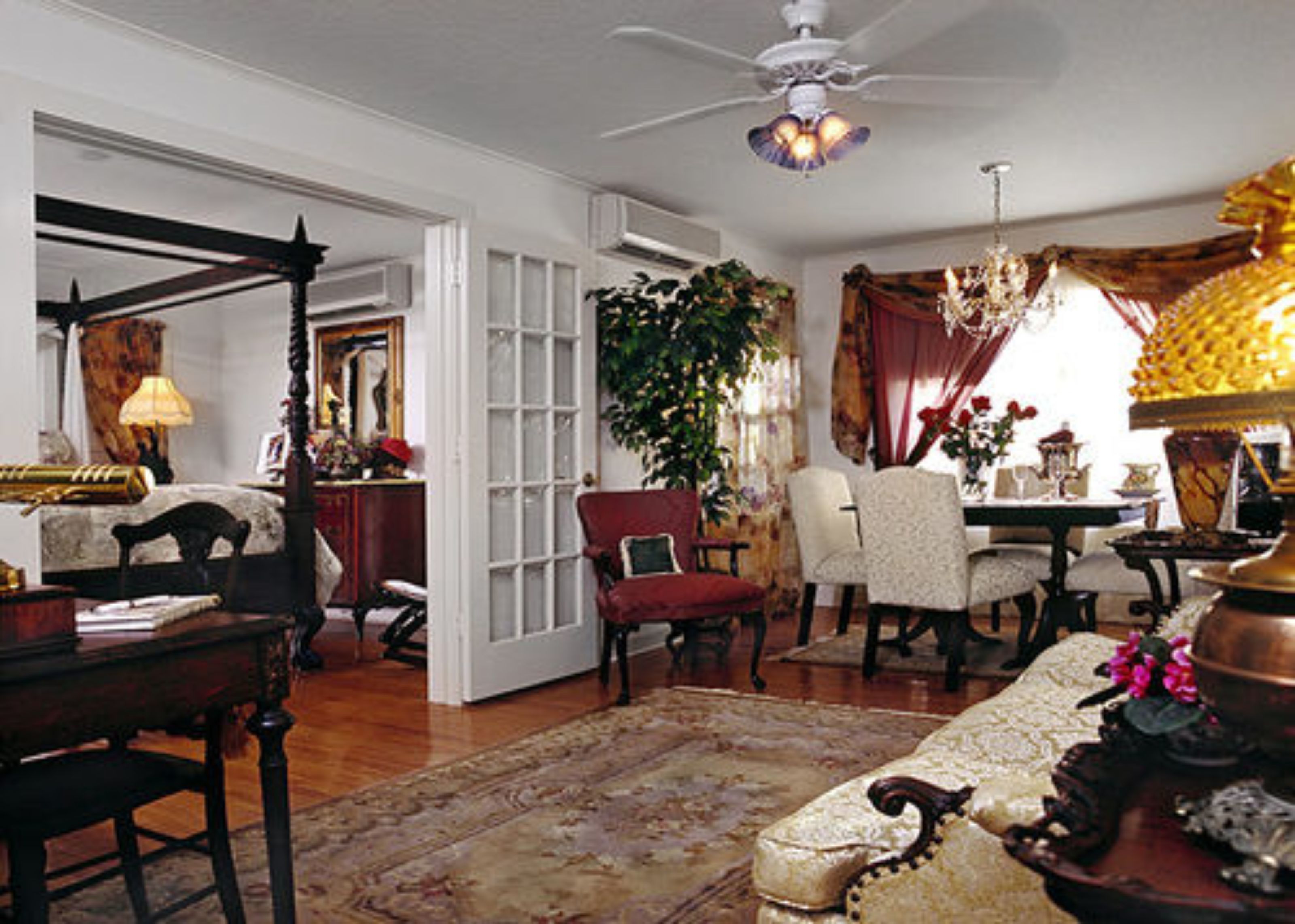 A traditional room with a four-poster bed, a chandelier, and a large window with curtains.