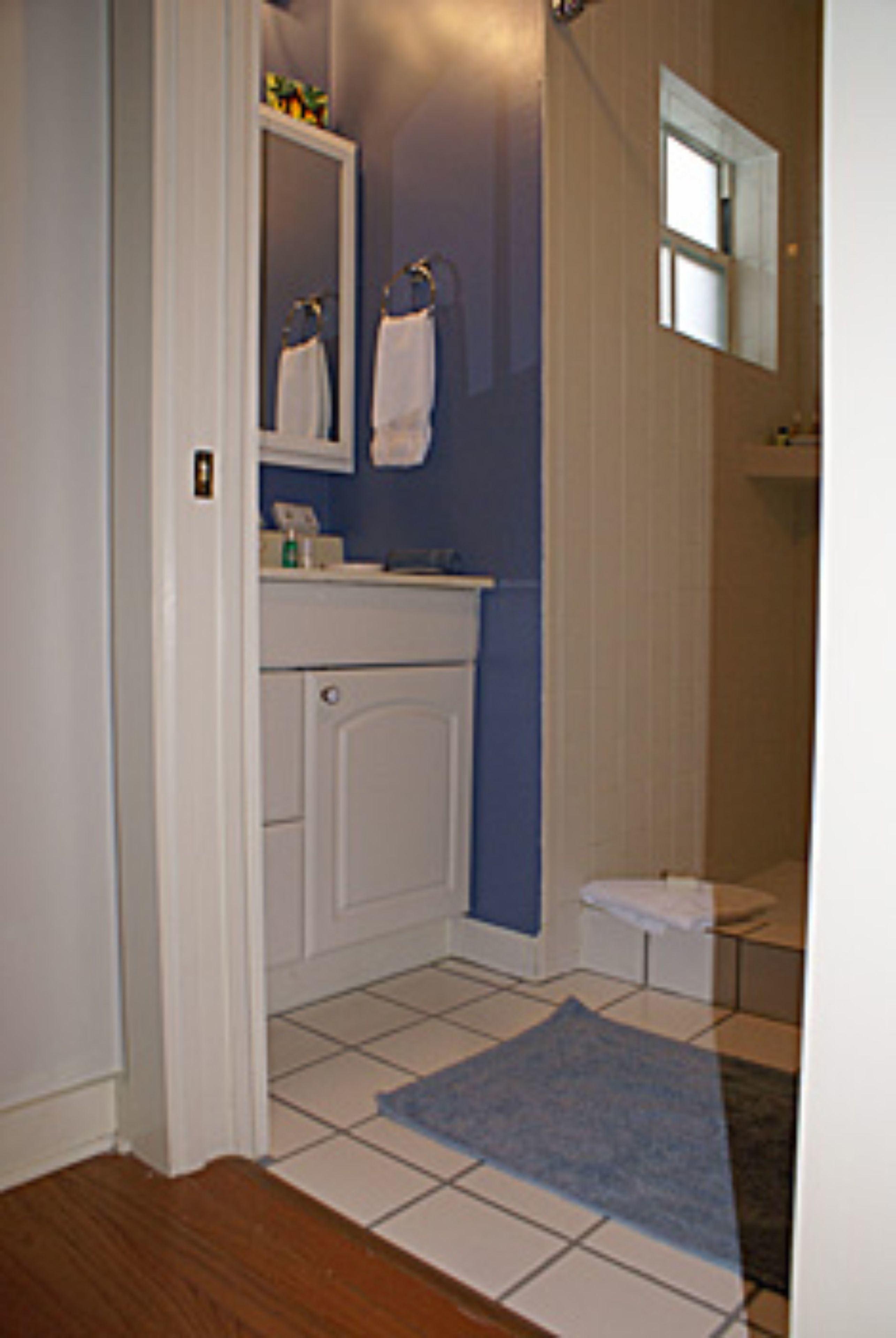 Un baño con tocador blanco, espejo, toallero y alfombra azul.