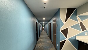 Passadís d'hotel amb un mosaic estampat, parets blaves i un disseny geomètric a la paret.