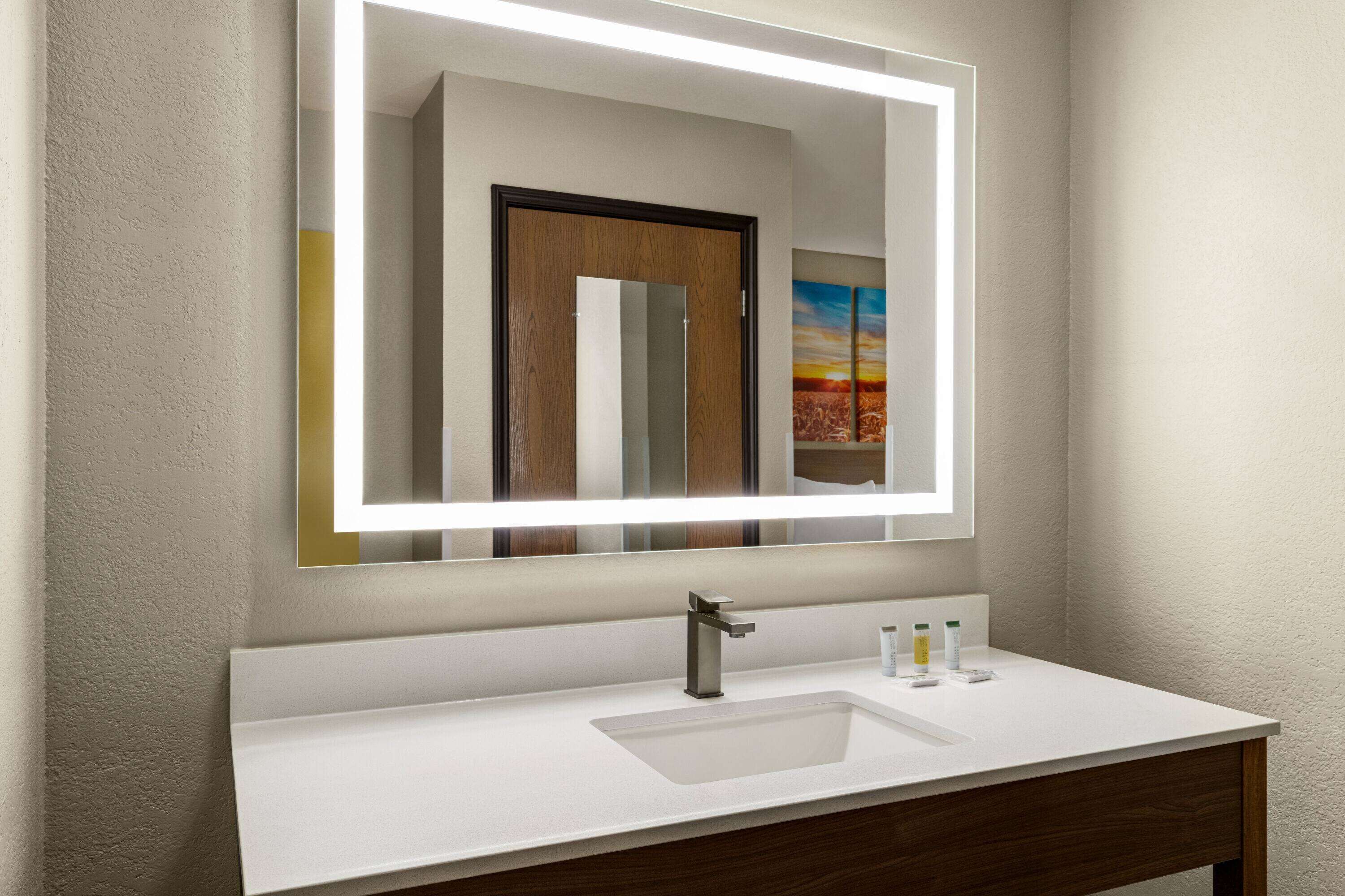 A modern bathroom with a white sink, a large mirror with integrated lighting, and a wooden vanity.