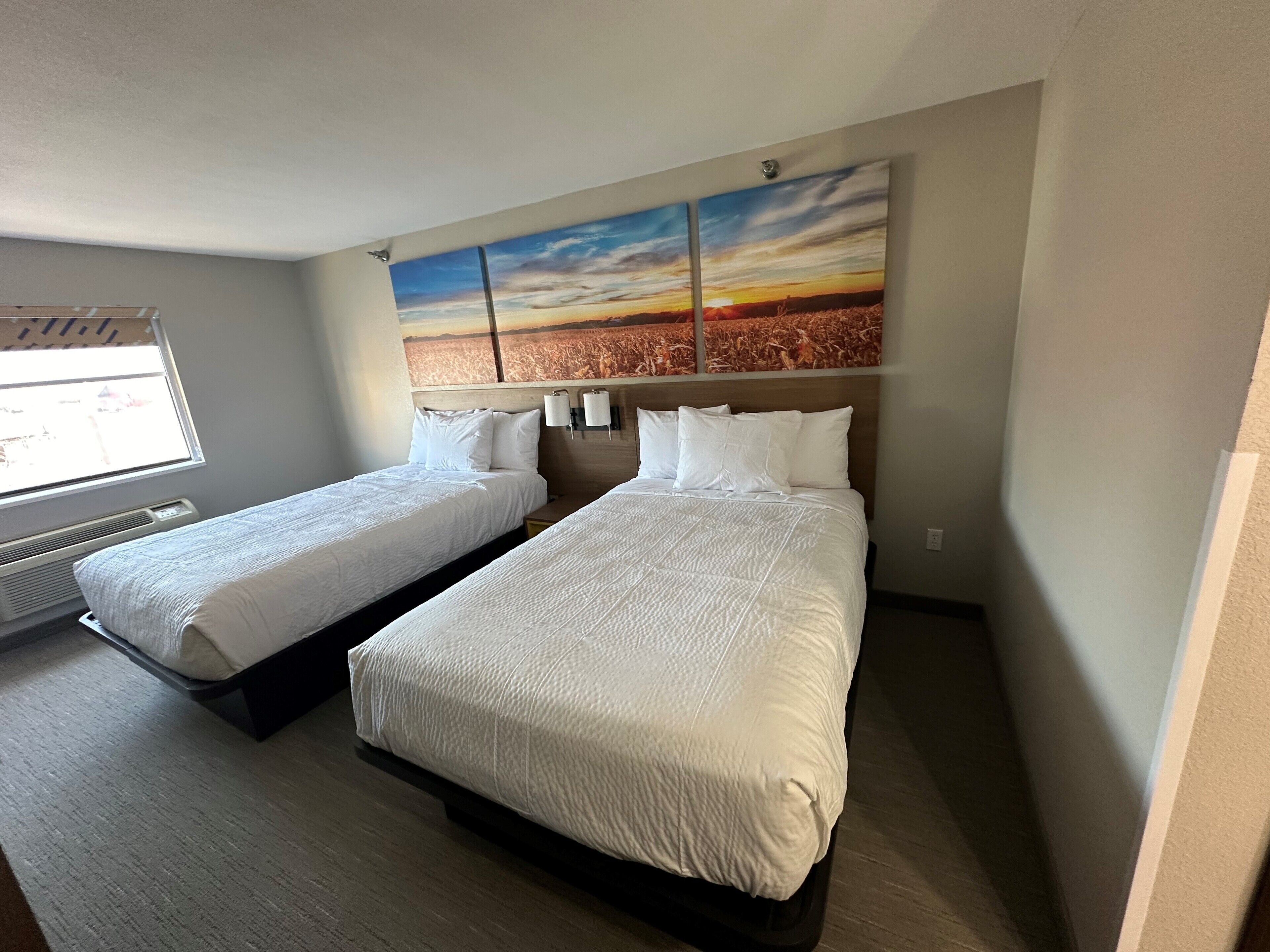 A hotel room with two beds, a large painting on the wall, and a window with a view of the outside.