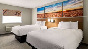 Habitació d'hotel amb dos llits, una finestra gran i una obra d'art penjada a la paret que representa un capvespre sobre un camp.