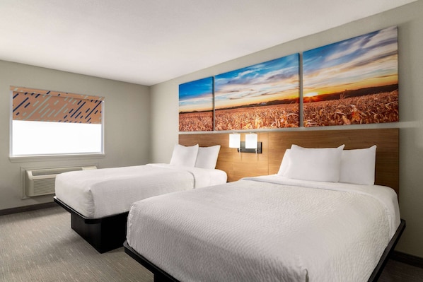 Habitación de hotel con dos camas, un ventanal grande y una obra de arte en la pared que muestra un atardecer sobre un campo.