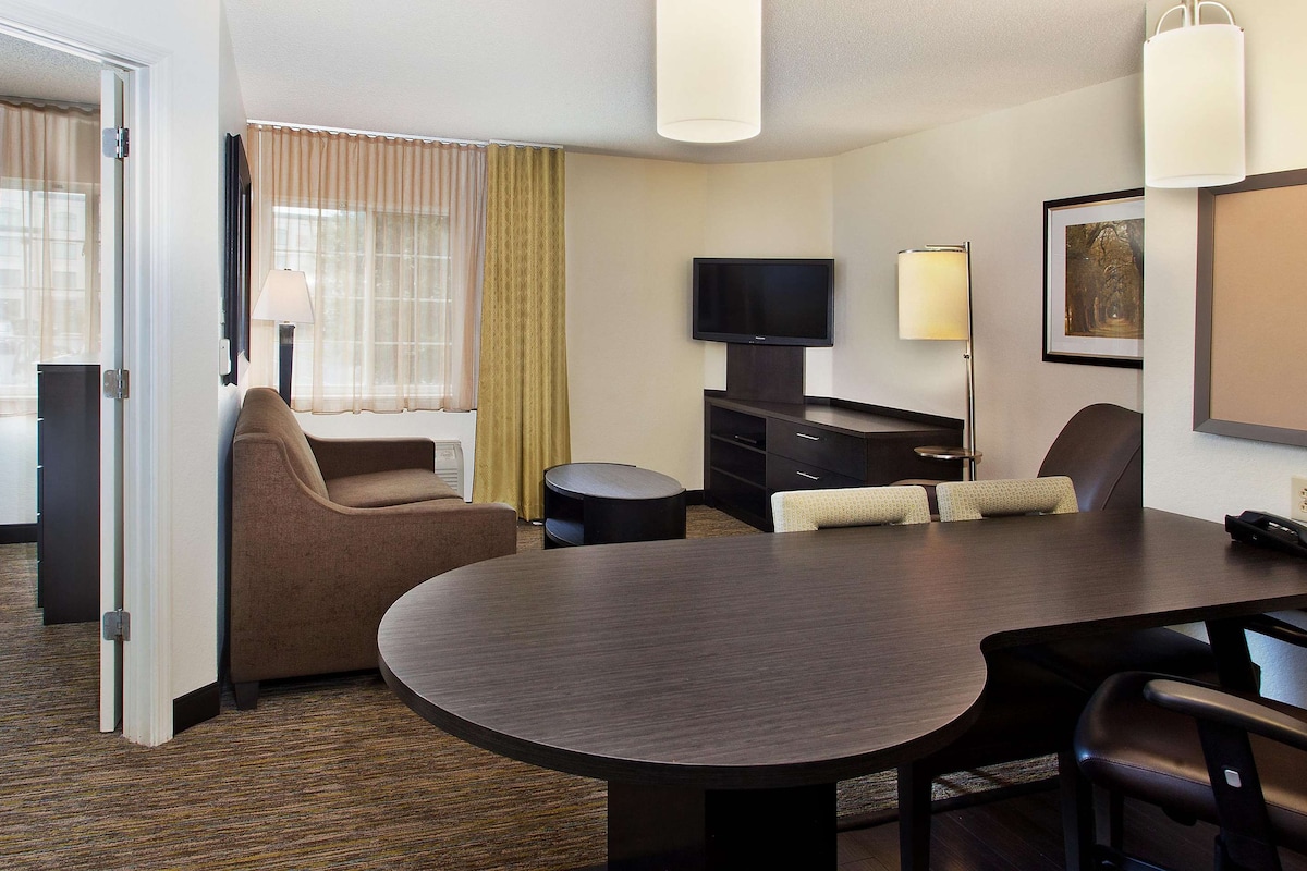 Una habitación de hotel con cama, zona de estar con mesa y sillas, televisor y lámpara.