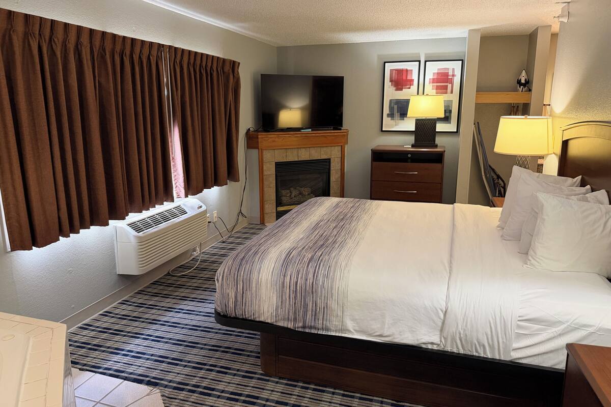 A hotel room with a bed, a flat-screen TV, a fireplace, a desk, and a lamp.