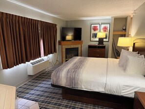 Habitación de hotel con cama, televisión de pantalla plana, chimenea, escritorio y lámpara.